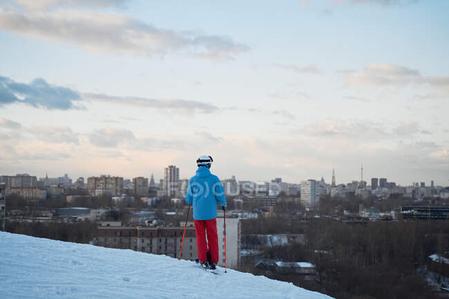Back view anonymous male skier in warm sportswear skiing along snowy hill slope in winter city park — Stock Photo