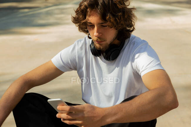 Retrato de un patinador mirando su teléfono. Tiene los auriculares en los hombros. - foto de stock