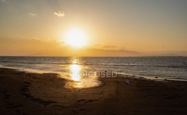 Мирный морской пейзаж на песчаном пляже возле спокойного моря на закате — стоковое фото