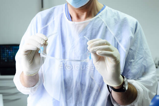 Cultivez médecin masculin méconnaissable dans des gants en latex avec des lunettes de sécurité au travail dans une clinique légère — Photo de stock
