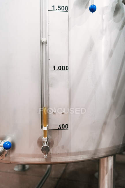 Serbatoio in acciaio inox con idrometro con numeri e scala contro liquido in tubo in fabbrica di birra — Foto stock
