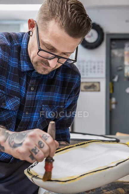Desde arriba del artesano tatuado aplicando pegamento en el asiento de la motocicleta mientras hace tapicería en el banco de trabajo - foto de stock