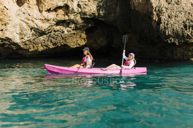 Вид сбоку путешественники с веслами, плавающие на бирюзовой морской воде возле скалистого берега в солнечный день в Малаге Испания — стоковое фото