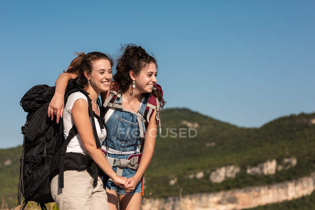 Delighted female hikers with backpacks in highlands and looking away while enjoying summer vacation — Stock Photo