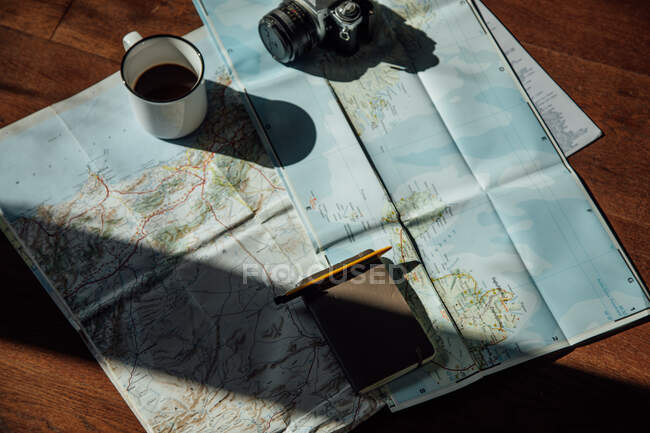 Top view of vintage photo camera and metal mug of coffee on route map during trip — Photo de stock