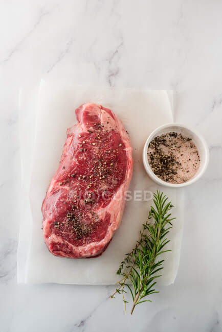 Overhead-Ansicht von rohem Fleischstück mit Thymianblättern gegen Backpapier auf Marmorgrund — Stockfoto