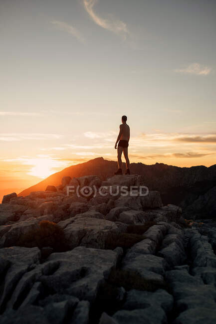 Side view anonymous male hiker in black underpants standing on rocky mountain summit and admiring spectacular highlands scenery at sunset — Stock Photo