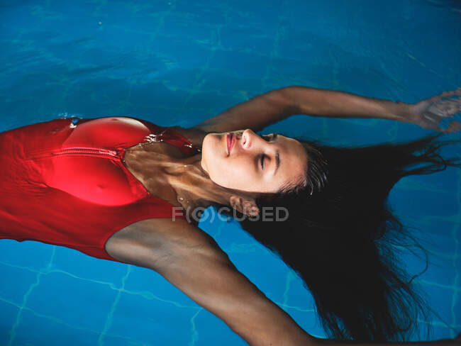 Зверху молода жінка-спортсменка в купальнику плаває на спині в басейні з чистою акваріумом і брижами — стокове фото
