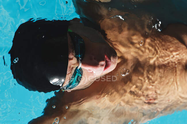 Вид зверху чоловіка-спортсмена в шапці для купання з піднятими руками, що плавають на спині в басейні під час тренувань — стокове фото