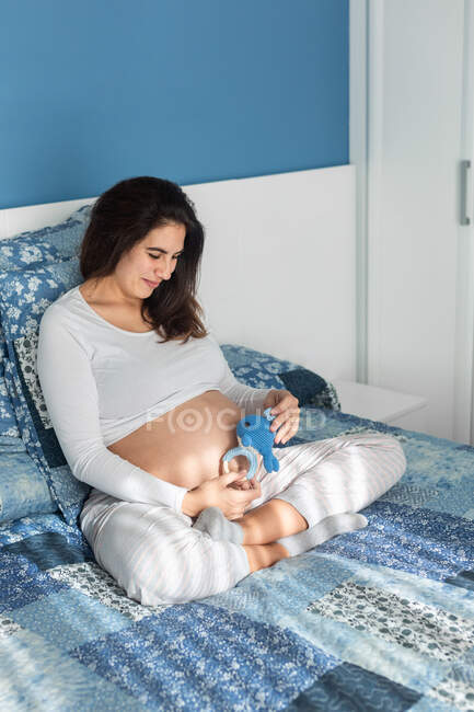 High angle of charming pregnant female sitting on soft bed and playing with plush toys — Stock Photo