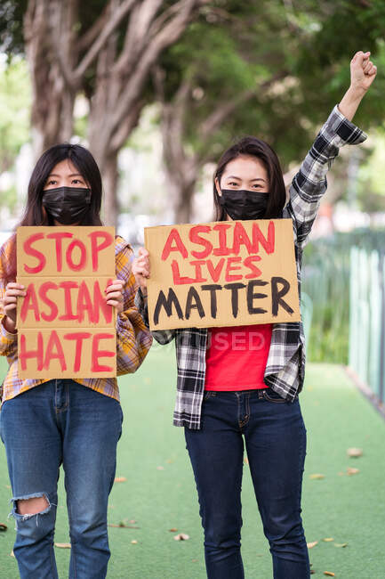 Етнічні жінки в масках тримають плакати, що протестують проти расизму на міській вулиці і дивляться на камеру — стокове фото
