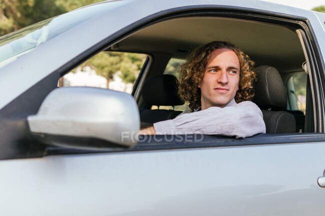 Щасливий молодий волохатий чоловік дивиться у відкритому вікні автомобіля, сидячи на водійському сидінні — стокове фото
