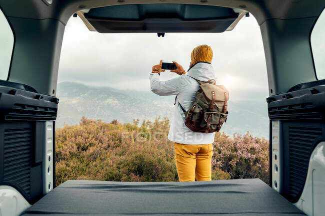 Вид з фургона невпізнаваного кемпера, що стоїть у високогір'ї та фотографує природу на мобільному телефоні — стокове фото