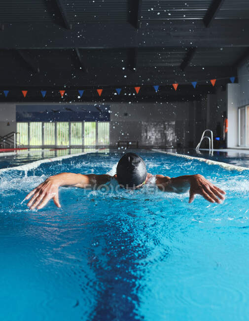 Nadador masculino forte na touca de banho que executa o curso da borboleta durante o exercício na piscina com água azul — Fotografia de Stock