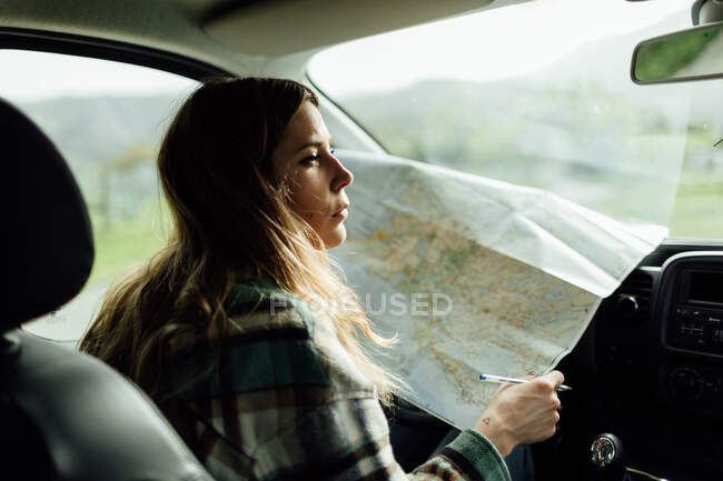 Вид збоку на жіночого туриста, який дивиться на карту маршруту, сидячи в автомобілі — стокове фото
