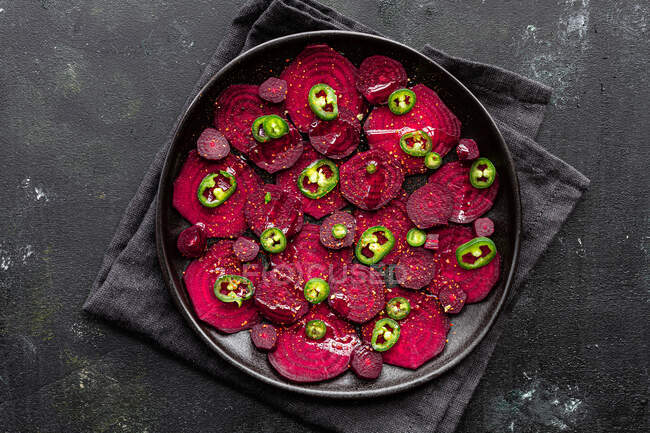 Top view composition of tasty beetroot slices arranged on baking pan with green jalapeno peppers and placed on black towel on kitchen table — Stock Photo