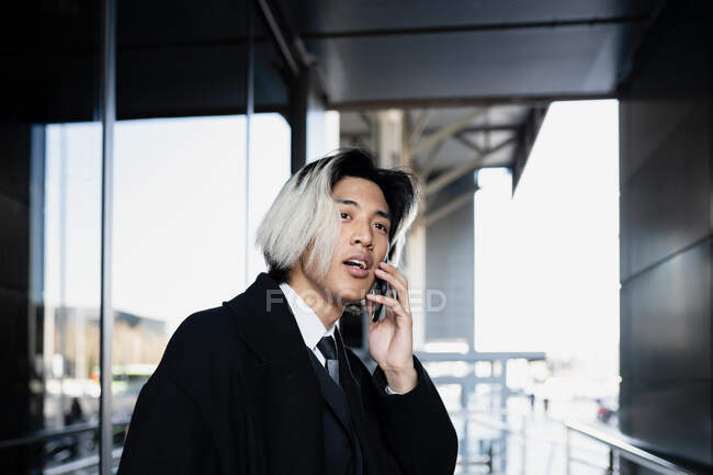 Jeune dirigeant masculin asiatique attentif en vêtements formels sur un appel téléphonique sur un smartphone en plein jour — Photo de stock