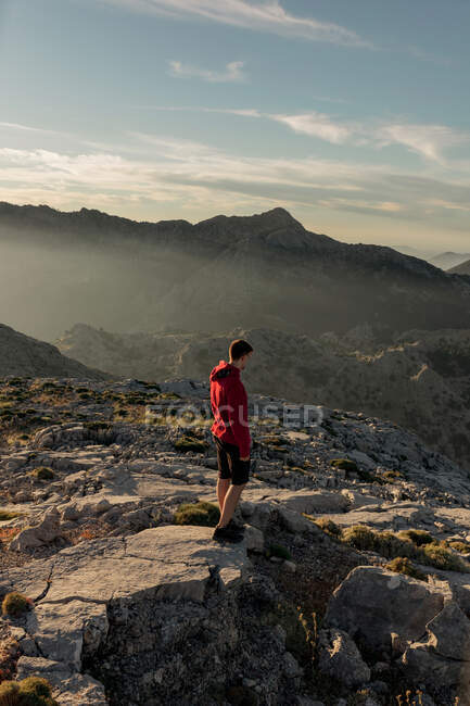 Невідомий чоловік - турист у повсякденному одязі, що відпочиває на скелястій горі і захоплюється мальовничими краєвидами над нерівними високогір 