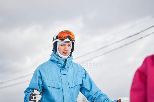 Радостный отец и дочь урожая в теплой спортивной одежде и шлемах стоя с лыжами на снежном склоне холма и глядя в сторону доволен — стоковое фото