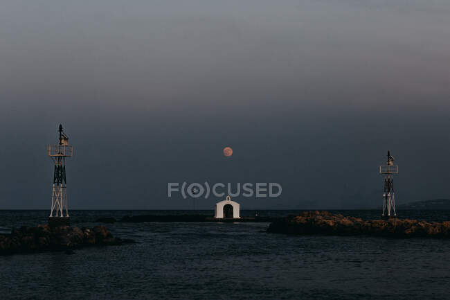 Сценічний вид на маленьку білу церкву Святого Ніколаса, розташовану на острові під темним небом, з яскравим місяцем у сутінках. — стокове фото