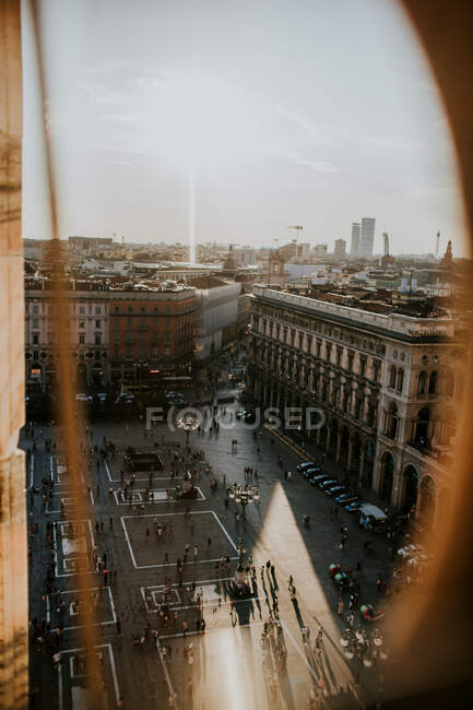 Through rounded hole view of aged multistory stone building exteriors and pavement with anonymous people under shiny sky in Milan Italy — Stock Photo