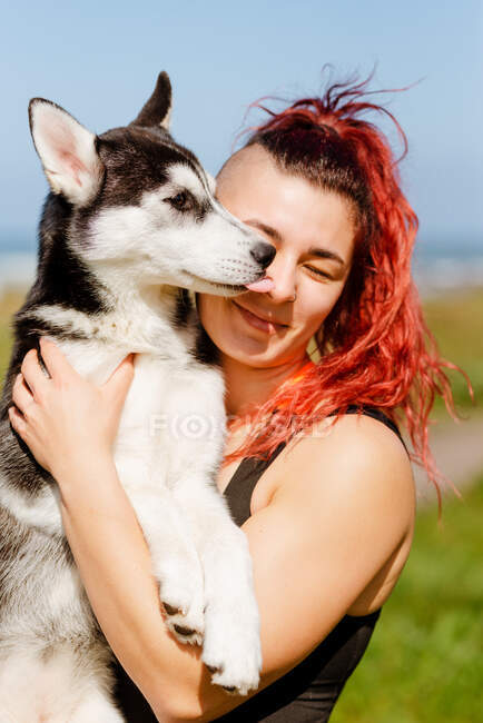 Contenuto atleta femminile con piercing abbracciando Siberian Husky con gli occhi chiusi alla luce del sole — Foto stock