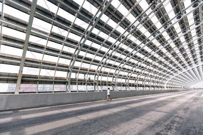 Homme méconnaissable debout dans un passage de verre inhabituel avec des murs géométriques courbes réfléchissant dans la flaque d'eau dans la ville urbaine — Photo de stock