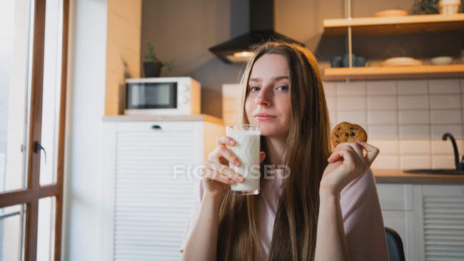 Fröhliche junge Frau mit leckerem Haferkeks mit Schokoladenchips zum Frühstück auf dem Tisch in der Küche — Stockfoto