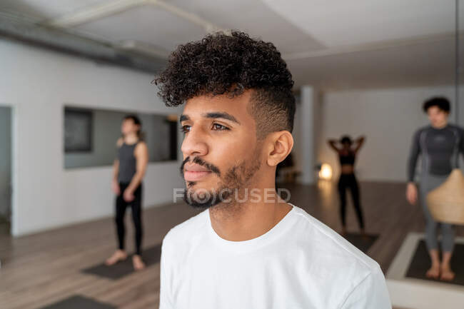 Konzentrierter afroamerikanischer Mann steht während des Yoga-Kurses mit multiethnischen Menschen im geräumigen Studio und schaut weg — Stockfoto