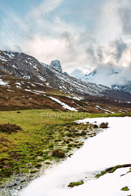 На мальовничих зелених полях із снігом у долині Піків Європи під важким хмарним небом в Іспанії. — стокове фото