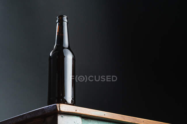Dark glass bottle of alcoholic drink on painted square shaped wooden table at home — Stock Photo