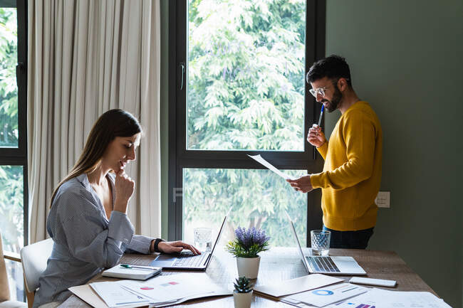 Glückliche junge Mitarbeiter versammeln sich mit Laptops am Schreibtisch und diskutieren Details von Dokumenten am modernen Arbeitsplatz — Stockfoto