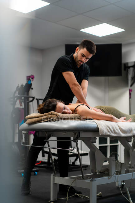 Неочікуваний чоловічий фізіотерапевт масажує спину жінки на ліжку під час медичної процедури в лікарні — стокове фото