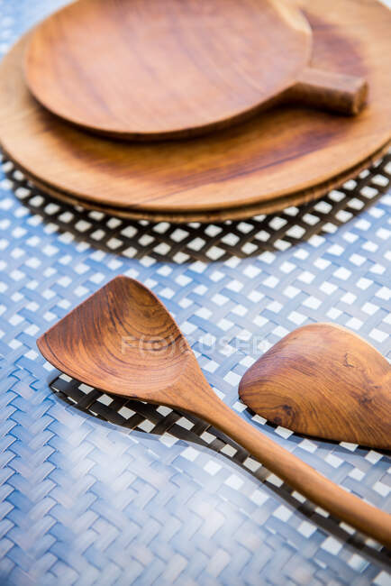 Сверху деревянные тарелки ручной работы и ложки, помещенные на плетеный стол из ротанга со стеклянным верхом при солнечном свете — стоковое фото