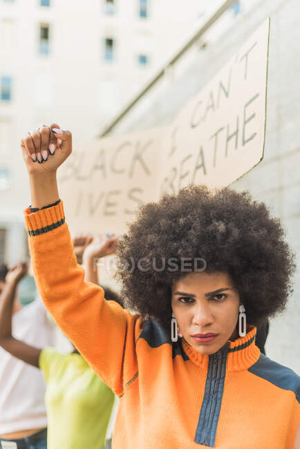 Young African American woman with afro hair standing with fist up protesting during Black Lives Matter demonstration in city — Fotografia de Stock