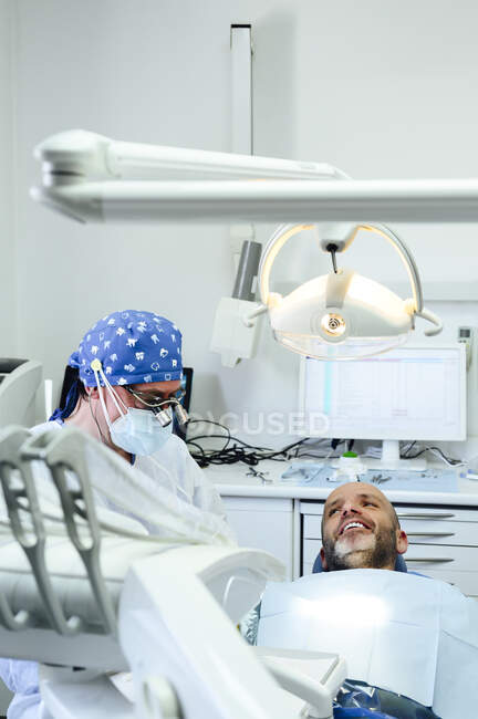 Side view of anonymous dental surgeon in uniform and medical binoculars with content man on chair in clinic — Stock Photo
