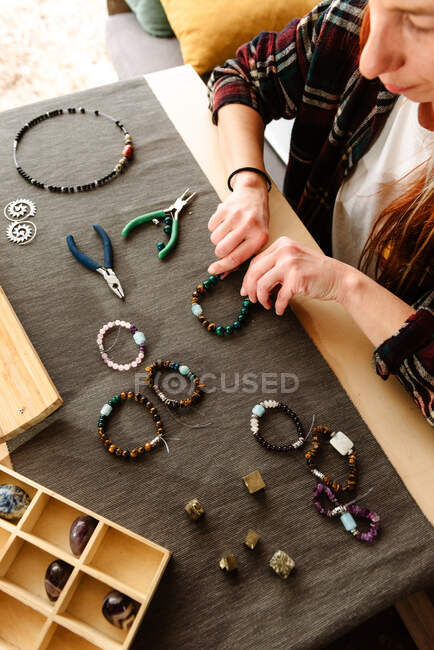 From above cropped unrecognizable female traveler sitting at table in truck and creating handmade bracelets during trip — Stock Photo