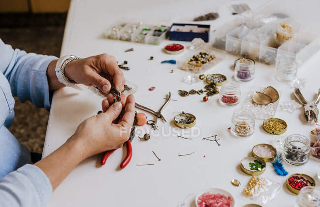 Высокий угол обрезки анонимных женщин-мастеров с инструментальным ожерельем за столом с различными инструментами — стоковое фото