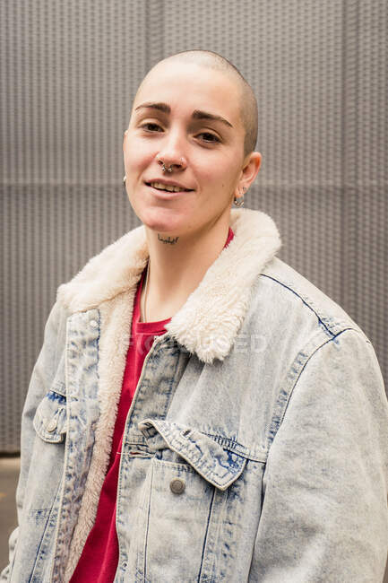 Happy transgender person in denim jacket with fur and earrings looking at camera in daylight — Stock Photo