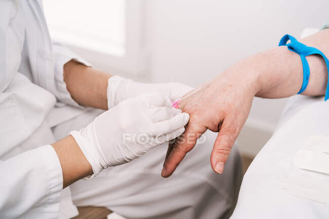 From above of crop unrecognizable medic in uniform preparing patient with tourniquet for intravenous procedure in hospital — Stock Photo