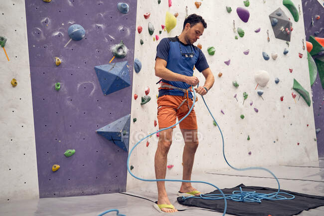 From below of male alpinist preparing ropes and harness for climbing in modern bouldering gym — Stock Photo