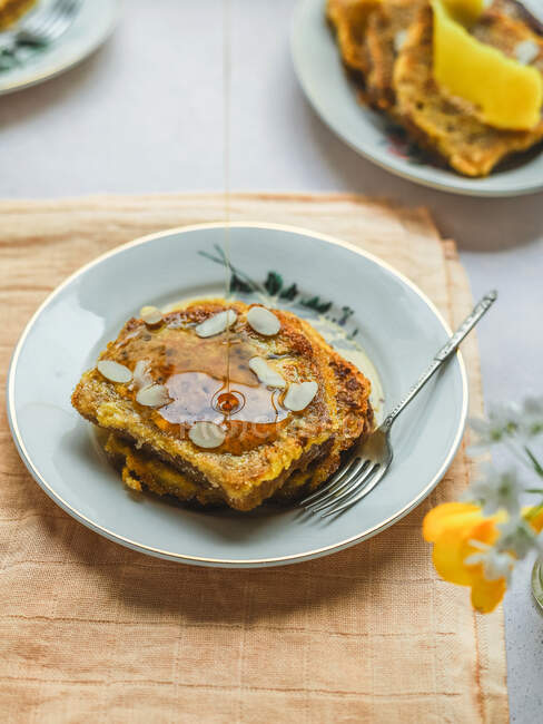 Von oben von leckerem französischem Toast, der mit Honig übergossen und mit Mandelflocken garniert auf einem Teller auf dem Tisch zum Frühstück serviert wird — Stockfoto