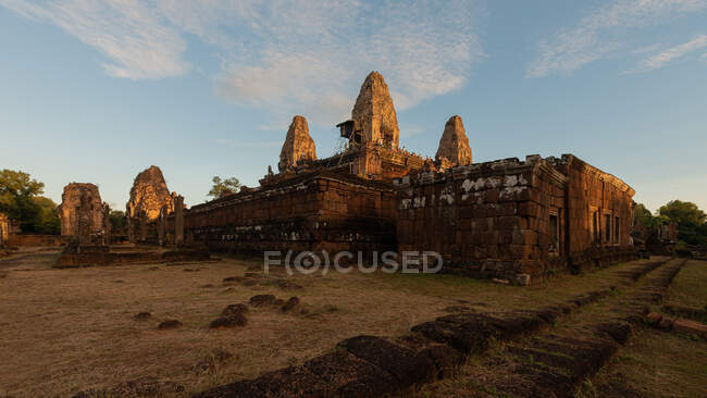 Aged stone temple complex exterior against lawn under blue sky in Cambodia in evening — Stock Photo