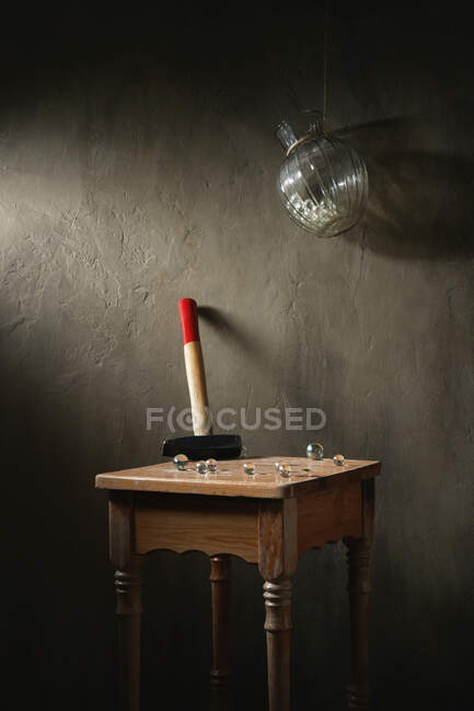 Hammer mit kleinen transparenten Kugeln auf hölzernem Vintage-Hocker unter hängender Vase auf Seil auf grauem Hintergrund — Stockfoto