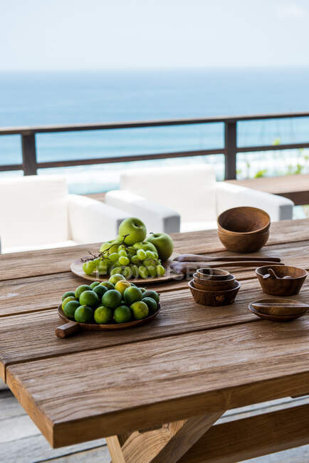 High angle plates with healthy delicious green limes with apples and grapes served on table with wooden bowl and spoons on terrace above sea on sunny day — Foto stock
