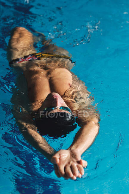 Male athlete in bathing cap with raised arms swimming on back in pool during training — Stock Photo
