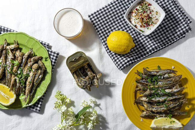 From above of traditional Spanish fried boquerones served on plates with lemons and bowl of white gazpacho soup placed on table with glass of beer in restaurant — Stock Photo