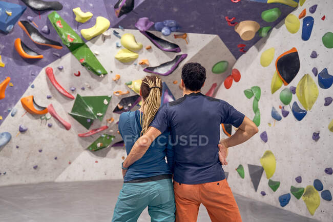 Обратный вид на неузнаваемую пару альпинистов, обнимающихся в современном альпинистском центре с искусственной стеной — стоковое фото