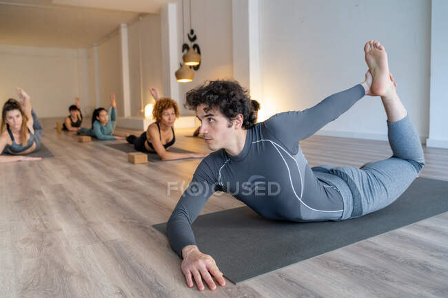 Treinador masculino flexível mostrando pose de arco para grupo de pessoas diversas durante a aula de ioga em estúdio — Fotografia de Stock