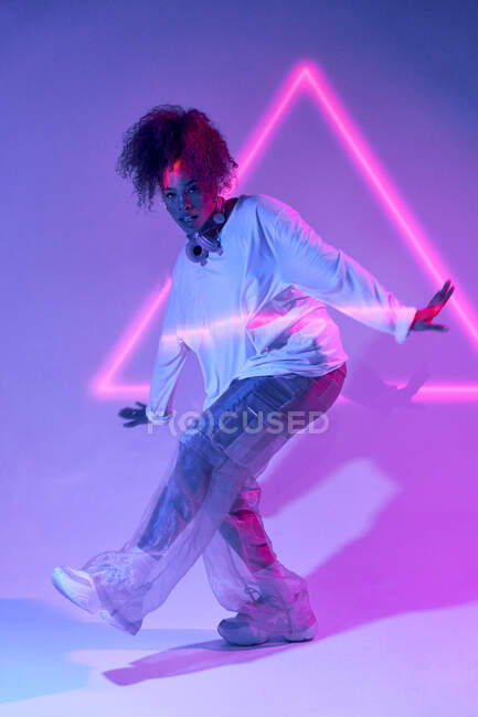 Full body talented young African American female dancer in loose clothes dancing in studio in neon lights and looking at camera — Stock Photo